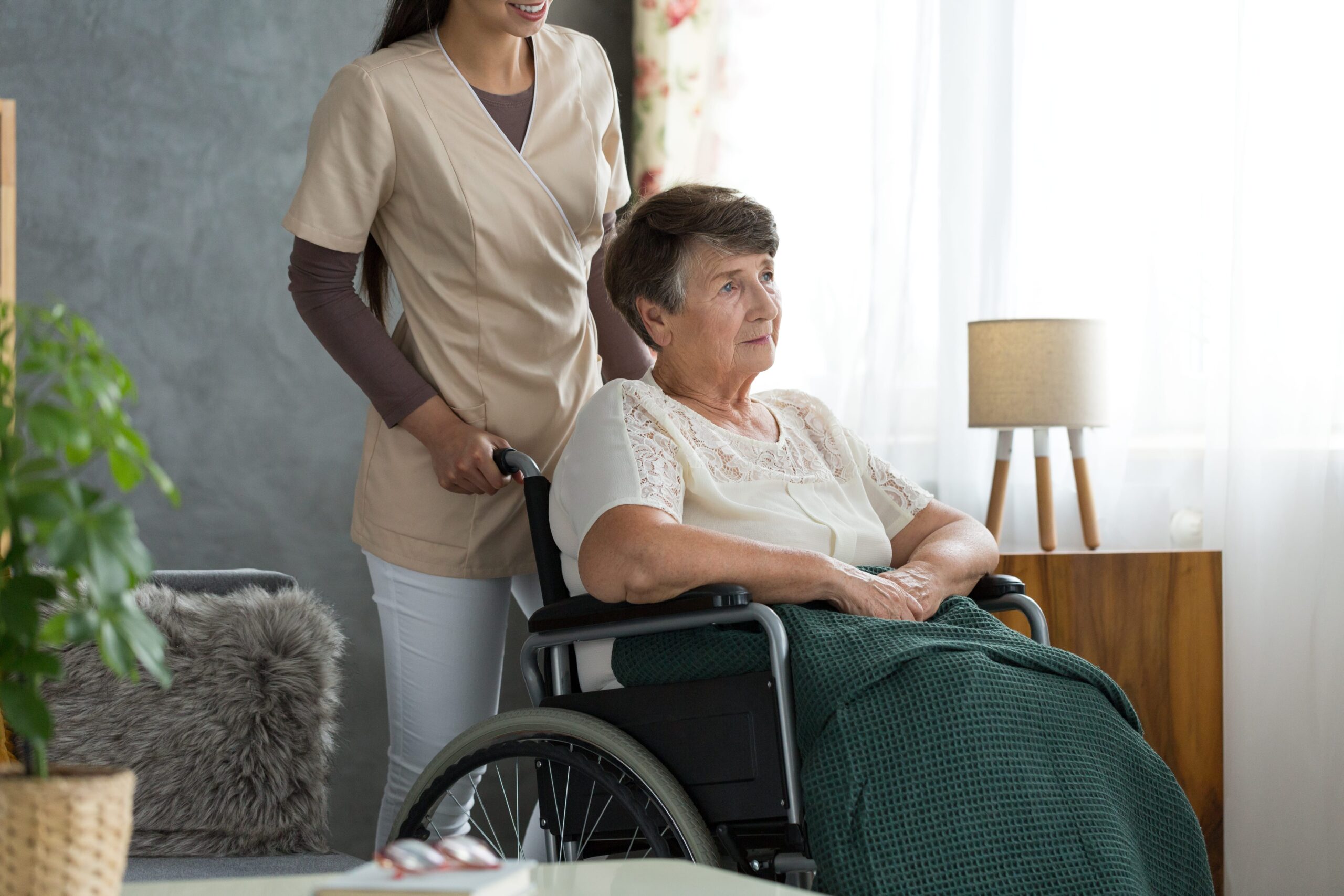 caregiver wheeling elderly woman to living room.